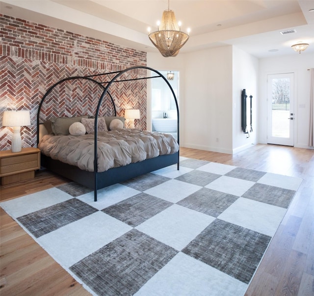 bedroom featuring a chandelier, an accent wall, brick wall, baseboards, and light wood-type flooring