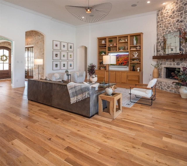 living room featuring light wood-style floors, a fireplace, arched walkways, and ornamental molding