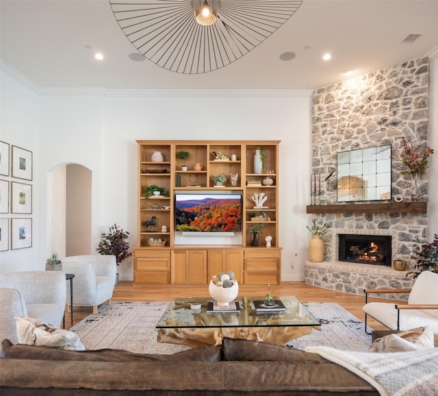 living room featuring light wood-style floors, a fireplace, arched walkways, and crown molding