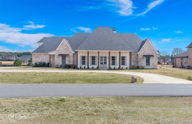 french provincial home featuring a front lawn, board and batten siding, a shingled roof, and brick siding