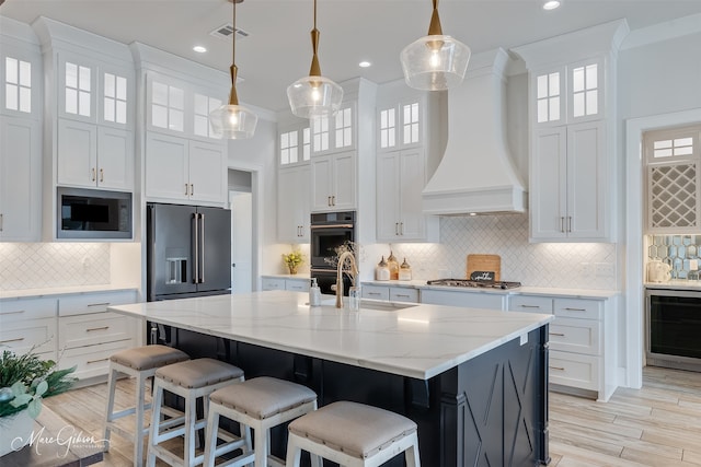 kitchen with stainless steel appliances, custom range hood, visible vents, a sink, and beverage cooler