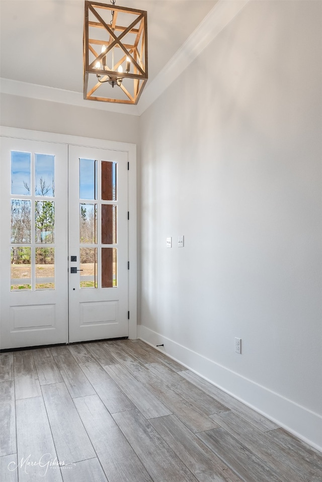 entryway featuring french doors, a notable chandelier, ornamental molding, wood finished floors, and baseboards