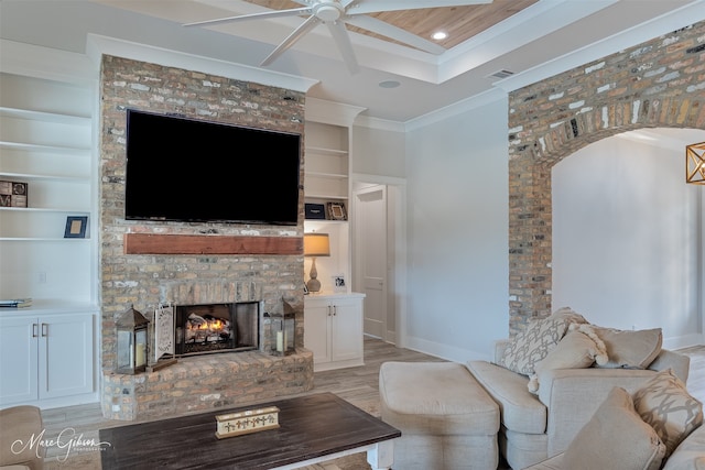 living area with baseboards, crown molding, light wood-type flooring, a brick fireplace, and built in shelves