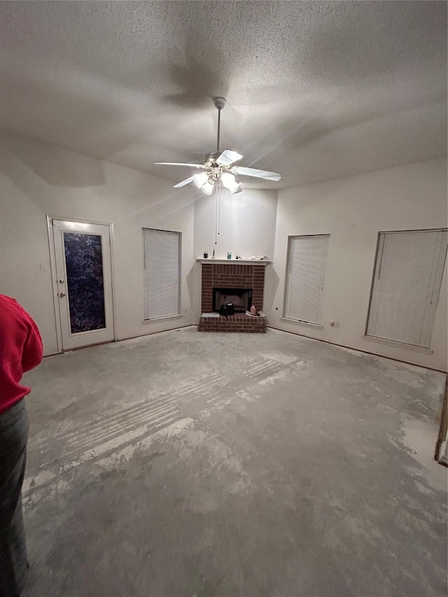 unfurnished living room featuring ceiling fan, a fireplace, a textured ceiling, and unfinished concrete floors