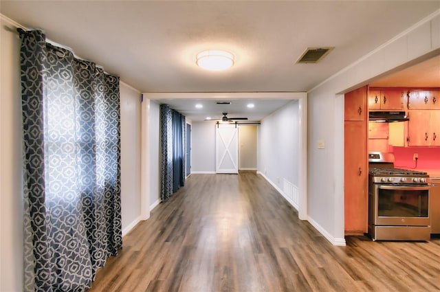 hall featuring wood finished floors, visible vents, baseboards, and a barn door