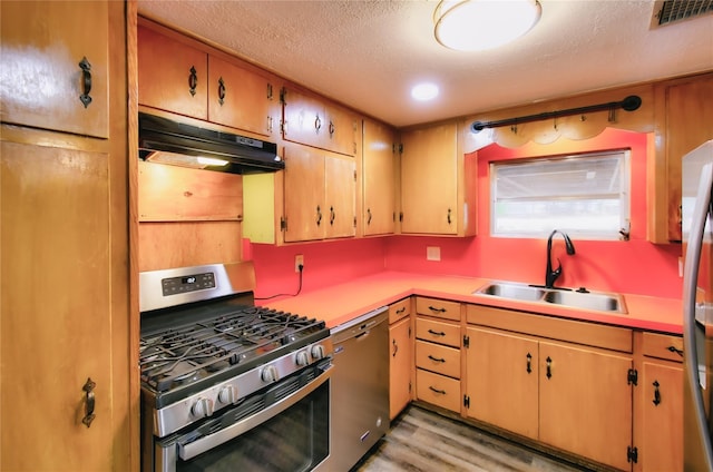 kitchen with under cabinet range hood, appliances with stainless steel finishes, light countertops, and a sink