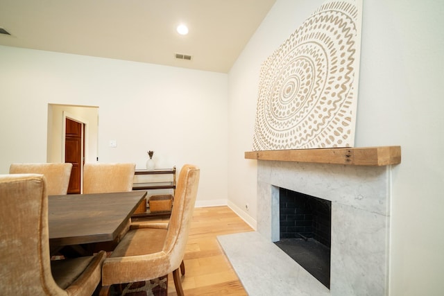 dining room featuring baseboards, visible vents, a premium fireplace, light wood-style floors, and recessed lighting