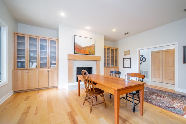 dining room featuring light wood-type flooring, a brick fireplace, visible vents, and recessed lighting