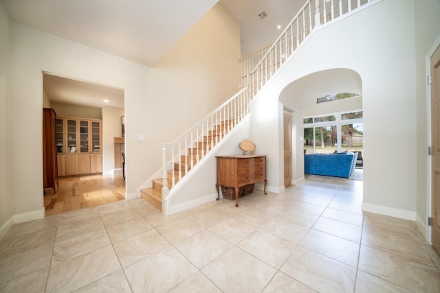 tiled entrance foyer featuring arched walkways, baseboards, a high ceiling, and stairs