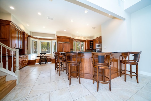 kitchen with dark countertops, visible vents, stainless steel microwave, and a kitchen breakfast bar