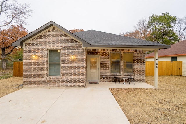 view of front of home featuring a patio, brick siding, roof with shingles, and fence