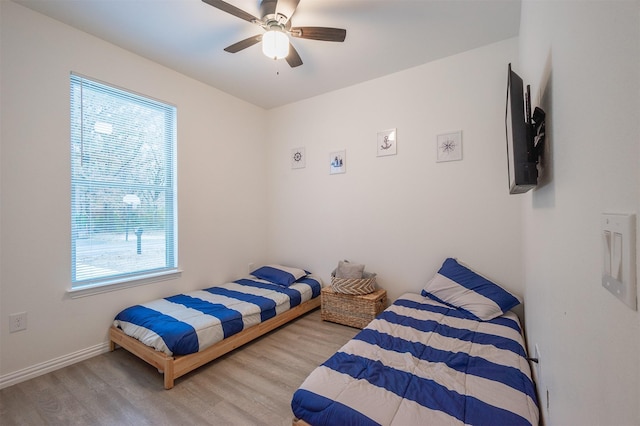 bedroom featuring a ceiling fan, multiple windows, baseboards, and wood finished floors