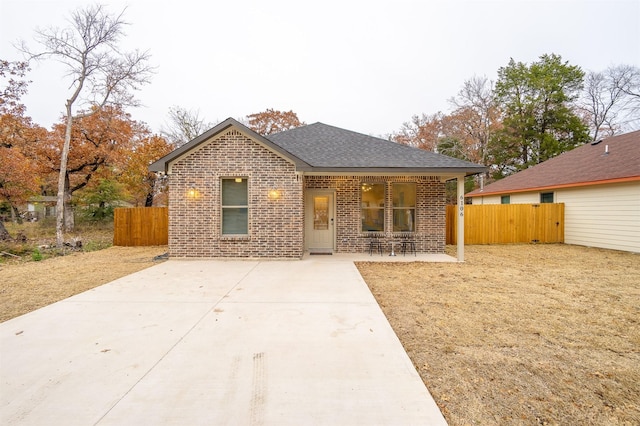 bungalow-style home with brick siding, a porch, a shingled roof, and fence