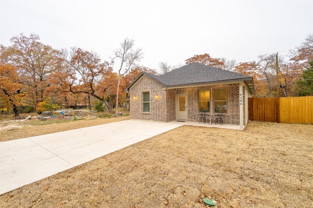 view of front of home with a shingled roof, brick siding, and fence