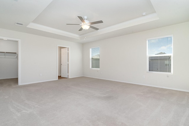 unfurnished bedroom with light colored carpet, visible vents, ornamental molding, a tray ceiling, and a walk in closet