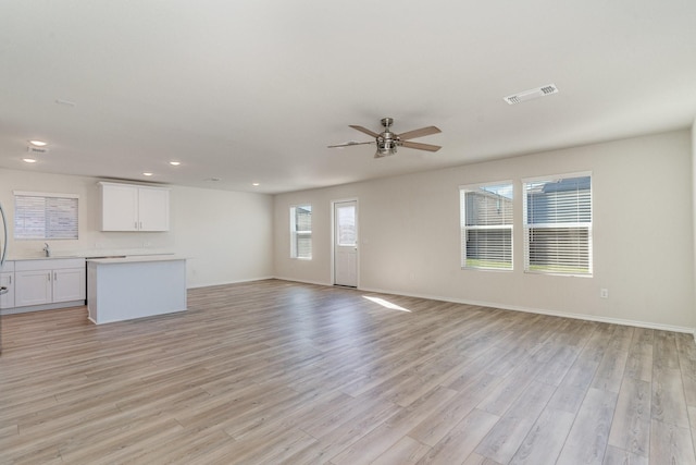 unfurnished living room with a sink, a ceiling fan, baseboards, visible vents, and light wood-style floors