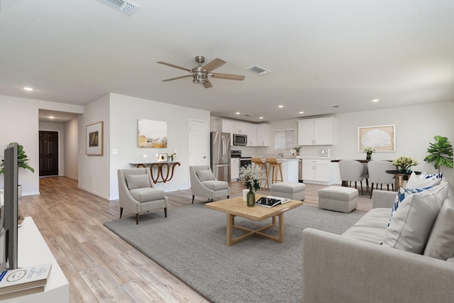 living room with light wood-type flooring, visible vents, baseboards, and recessed lighting