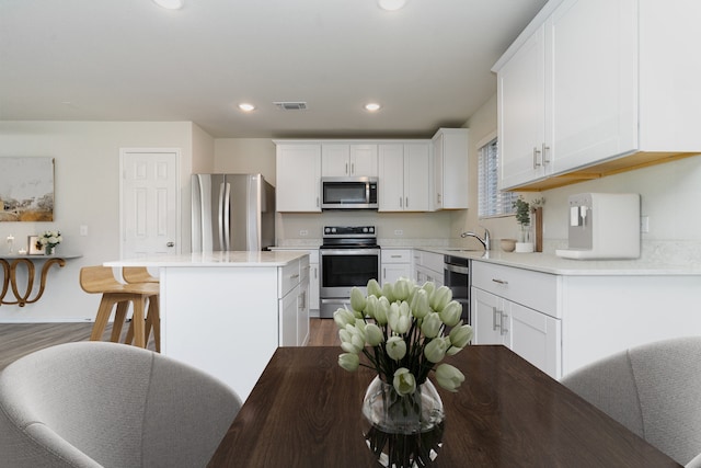 kitchen with visible vents, appliances with stainless steel finishes, white cabinets, a kitchen island, and a sink