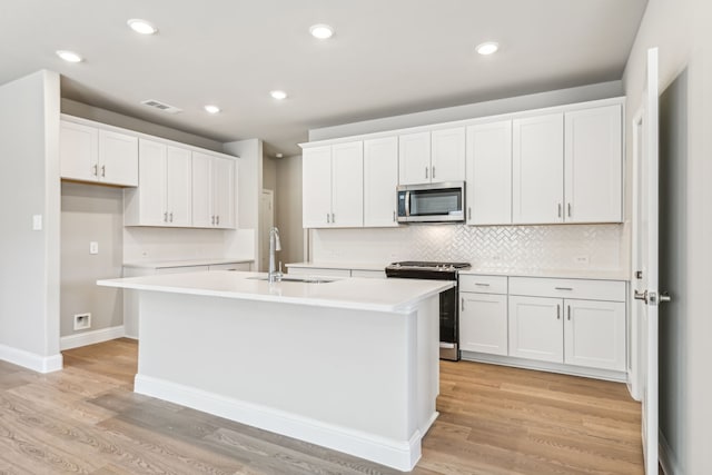 kitchen with visible vents, white cabinets, an island with sink, stainless steel appliances, and a sink