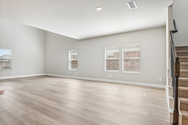 unfurnished living room with baseboards, stairway, visible vents, and light wood-style floors