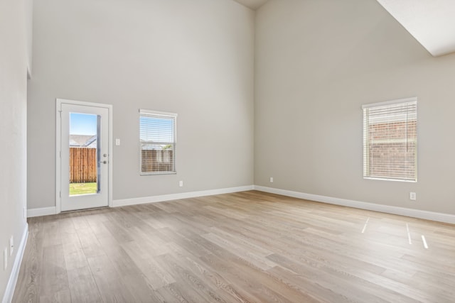 spare room featuring a towering ceiling, light wood-type flooring, and baseboards