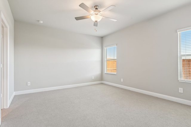 spare room featuring a ceiling fan, light carpet, and baseboards