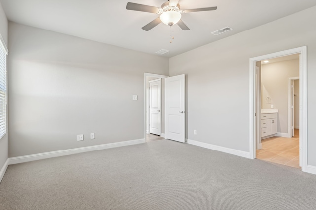 unfurnished bedroom featuring baseboards, visible vents, connected bathroom, light colored carpet, and ceiling fan