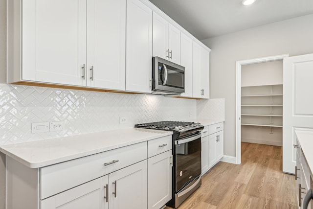 kitchen featuring light wood finished floors, decorative backsplash, appliances with stainless steel finishes, light countertops, and white cabinetry