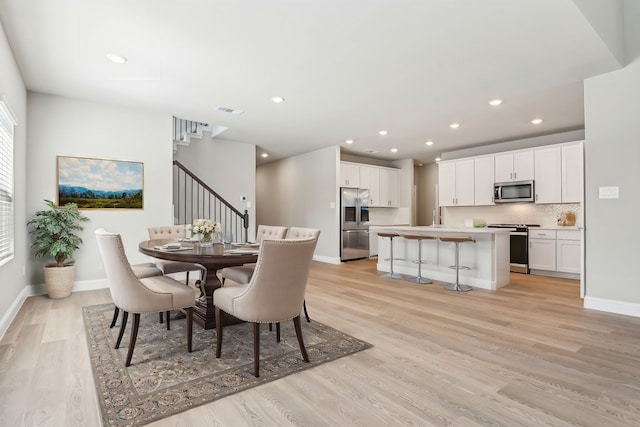 dining room with light wood finished floors, baseboards, stairway, and visible vents