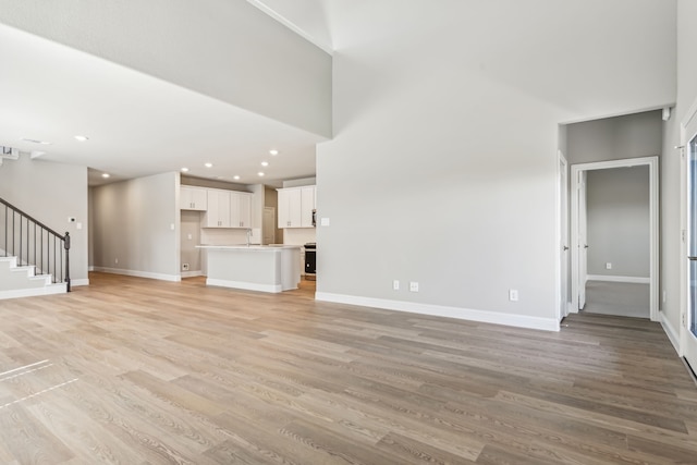 unfurnished living room with light wood-style floors, a towering ceiling, baseboards, and stairs