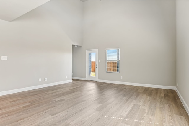 empty room featuring light wood finished floors, a high ceiling, and baseboards