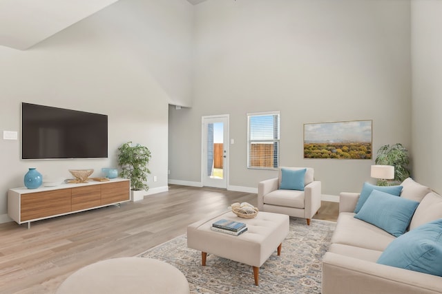 living room featuring light wood-type flooring, a high ceiling, and baseboards