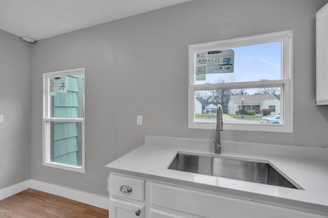 kitchen with white cabinetry, light countertops, baseboards, and a sink