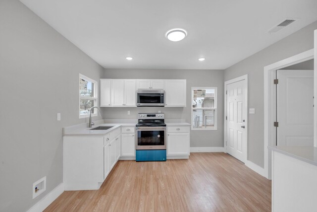 kitchen with light wood-type flooring, visible vents, a sink, stainless steel appliances, and light countertops