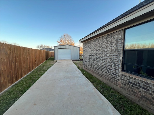 view of home's exterior featuring a garage, concrete driveway, fence, an outdoor structure, and brick siding