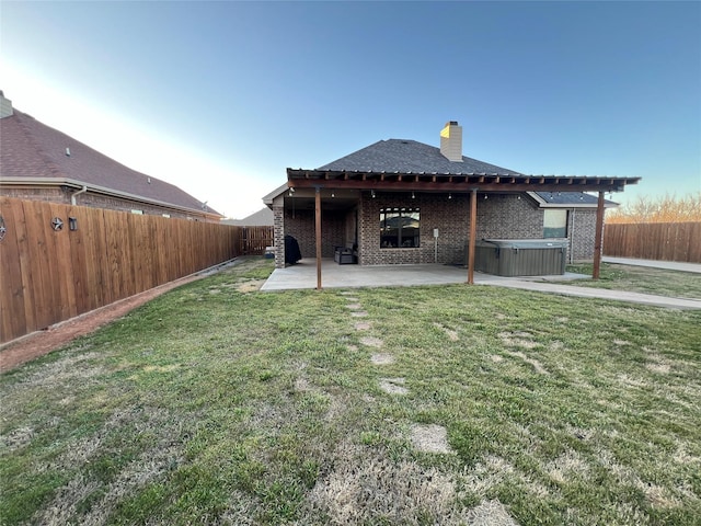 rear view of property with a fenced backyard, brick siding, a yard, a patio area, and a hot tub