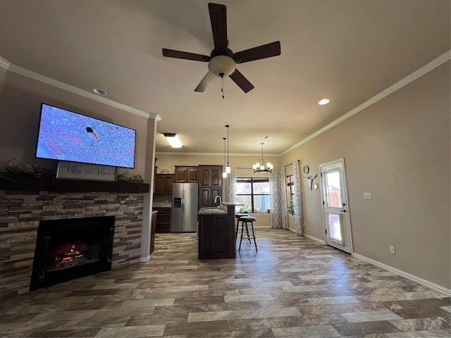 kitchen with a fireplace, a kitchen breakfast bar, ornamental molding, stainless steel fridge, and a center island with sink