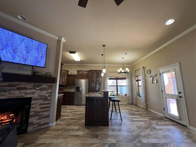 kitchen with a stone fireplace, a breakfast bar, a sink, stainless steel fridge with ice dispenser, and crown molding