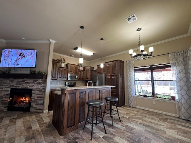 kitchen featuring stainless steel appliances, visible vents, ornamental molding, a stone fireplace, and an island with sink