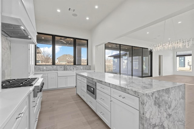 kitchen featuring appliances with stainless steel finishes, white cabinetry, a kitchen island, a sink, and premium range hood