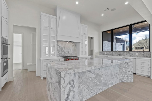 kitchen with custom exhaust hood, visible vents, stove, stainless steel double oven, and white cabinetry