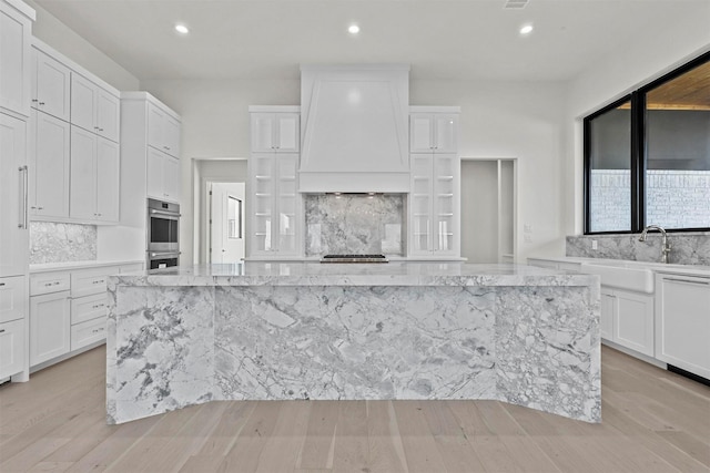 kitchen with stainless steel appliances, custom range hood, white cabinetry, and a fireplace