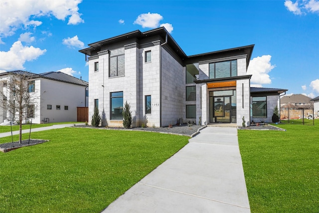 modern home featuring a front yard, concrete block siding, and fence