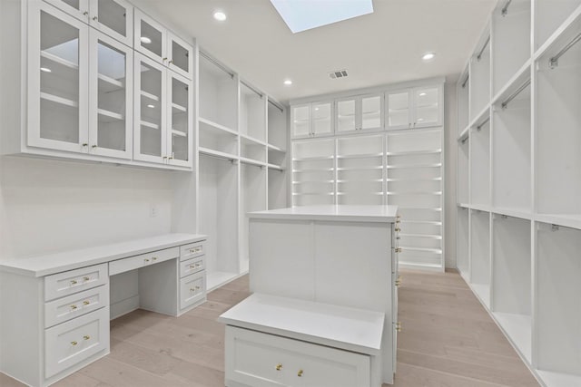 walk in closet with light wood-type flooring, a skylight, and visible vents