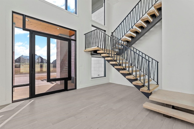 stairway with wood finished floors, a towering ceiling, and baseboards