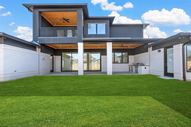 rear view of house featuring a ceiling fan, a patio area, a lawn, and exterior kitchen