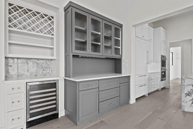 kitchen with light wood finished floors, wine cooler, glass insert cabinets, gray cabinets, and light countertops