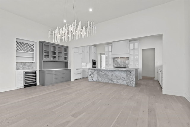 unfurnished living room with light wood finished floors, beverage cooler, baseboards, a high ceiling, and a chandelier