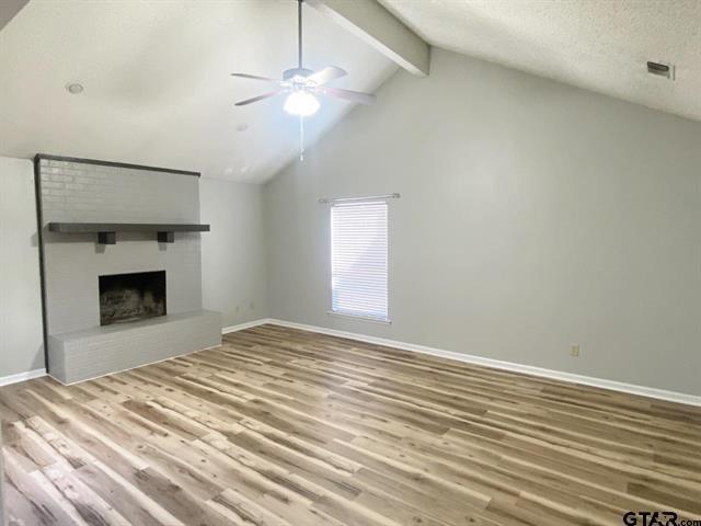 unfurnished living room with wood finished floors, lofted ceiling with beams, ceiling fan, a fireplace, and baseboards