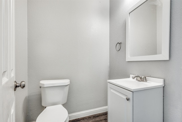 half bathroom featuring toilet, baseboards, wood finished floors, and vanity